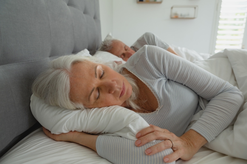 3 Health Benefits for Using Your AC While Sleeping. Senior couple sleeping together in bed in bedroom.