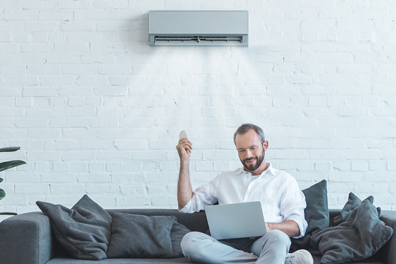 4 Amazing Benefits of Ductless Units. Man turning on his ductless unit while on his couch.