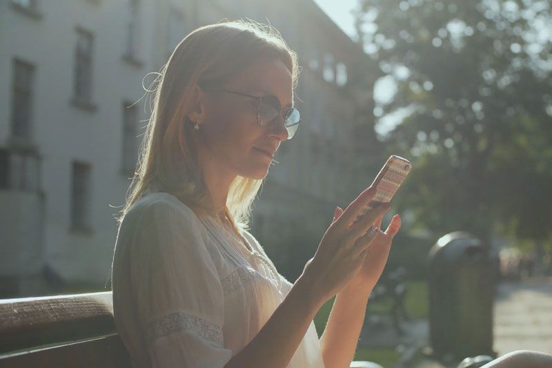 A woman wearing sunglasses looks at her phone. Are Wi-Fi Thermostats Cost-Effective?